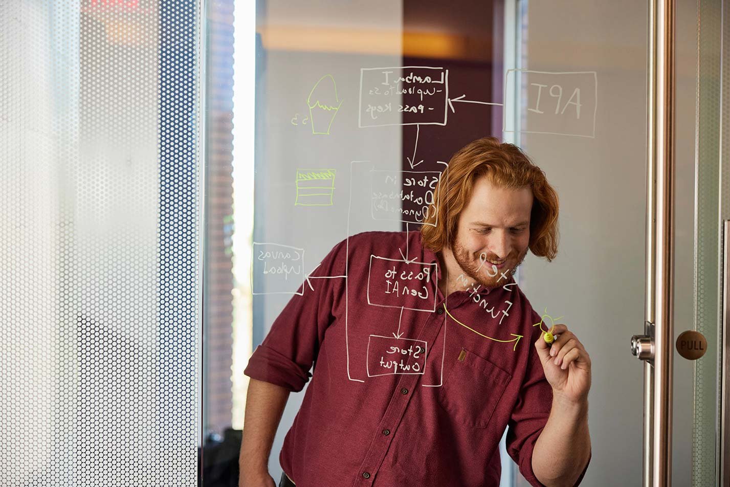 A man draws a diagram on a transparent door, showcasing problem-solving skills in ASU's Artificial Intelligence in Business degree.