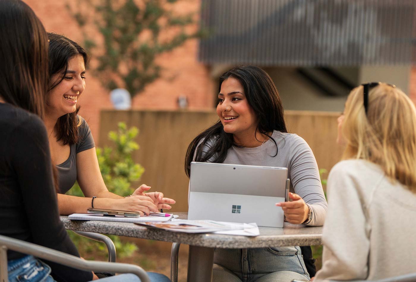 At an outdoor table, a laptop discussion brings an study group together, highlighting the valuable connections made in ASU's Business (Communication) degree.