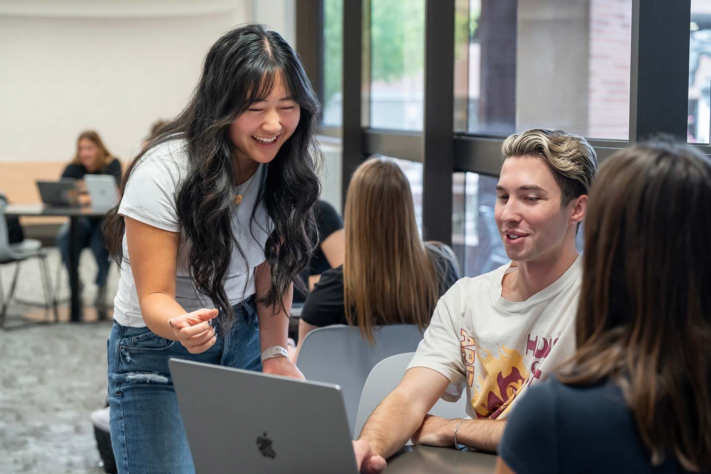 Students engage in a discussion around a laptop in a modern study space, highlighting teamwork within ASU's Economics degree.