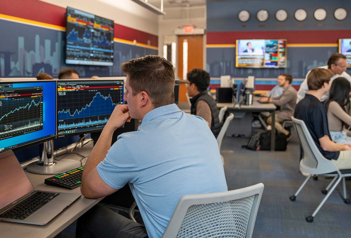 A student analyzes financial data across multiple screens, showcasing practical learning in ASU's PhD in Finance program.