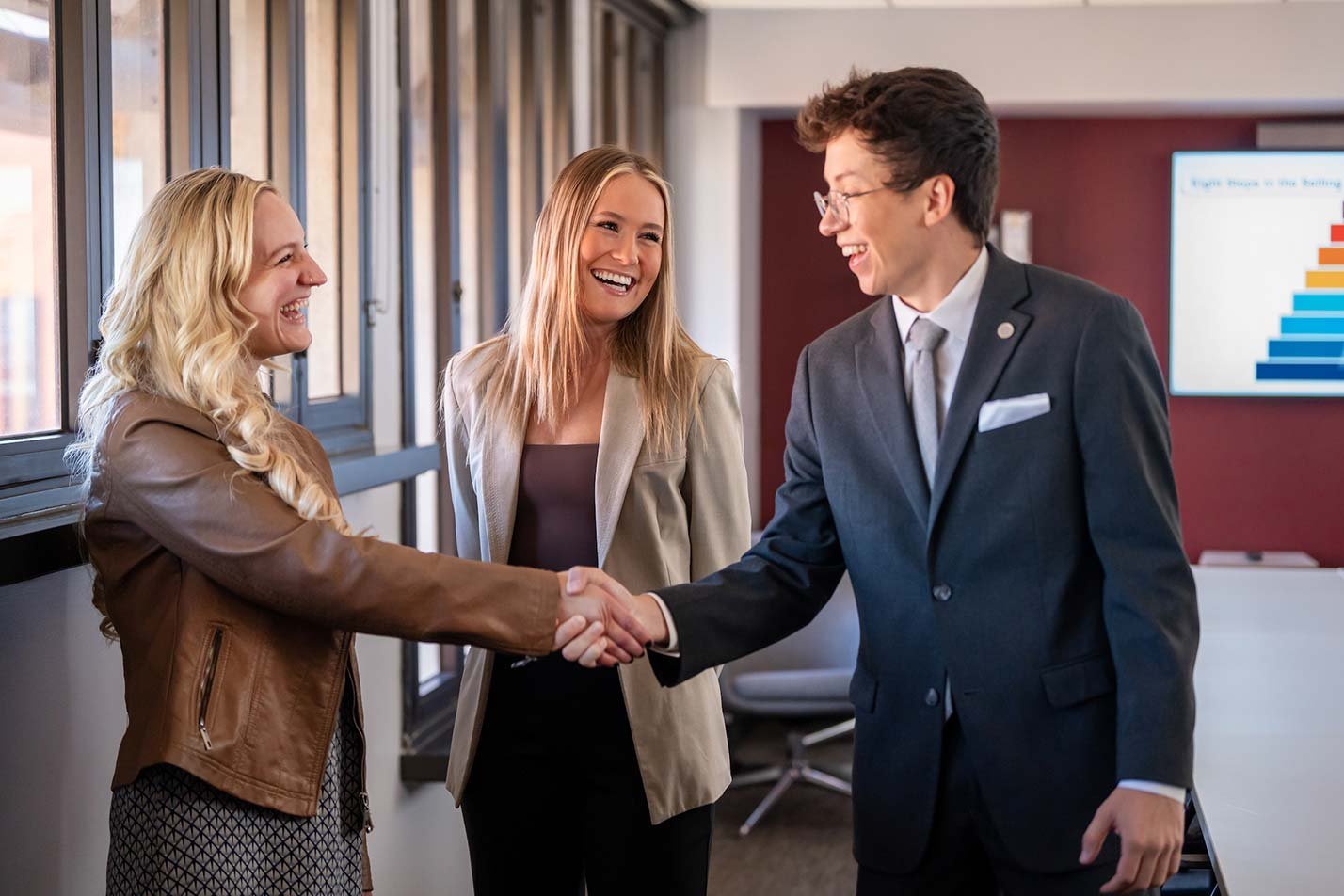 A friendly handshake in a modern office setting illustrates negotiation skills gained through ASU's Marketing (Professional Sales) degree.