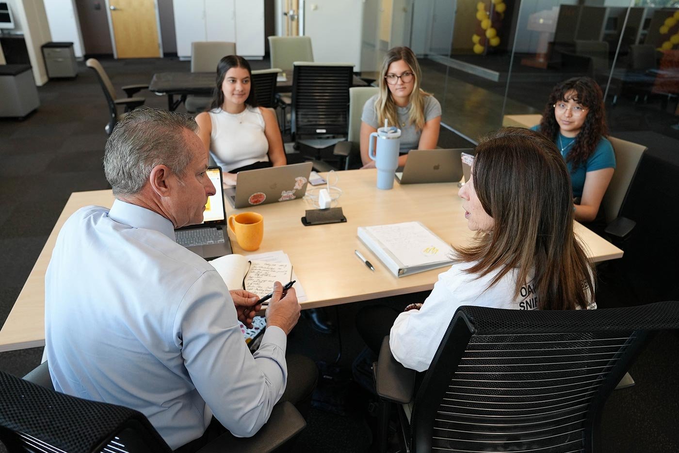 Students around a table talk about research strategies, highlighting interactive learning in ASU's PhD in Journalism and Mass Communication program.