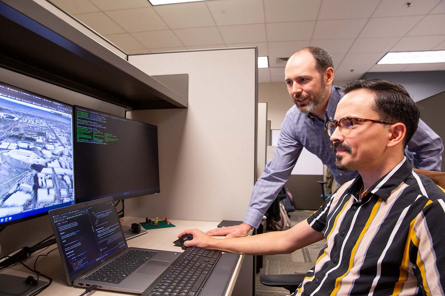 A professor guides a student through coding in a modern office, reflecting ASU's Artificial Intelligence Engineering (Human-Centered Artificial Intelligence), MS program.