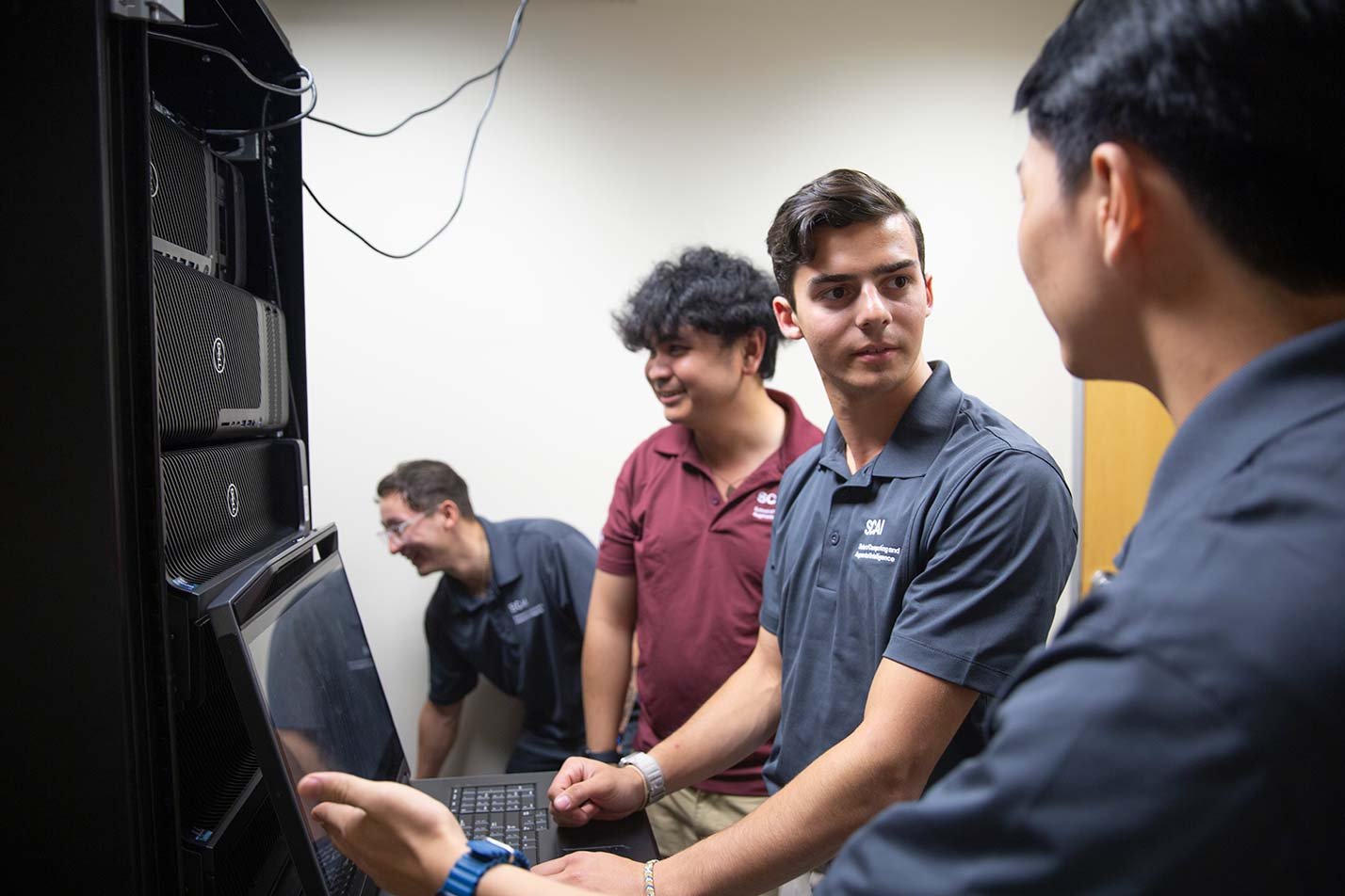 Graduate students discuss ideas while working on a laptop in a server room, demonstrating teamwork in ASU's MS in Artificial Intelligence Engineering (Software Engineering) program.