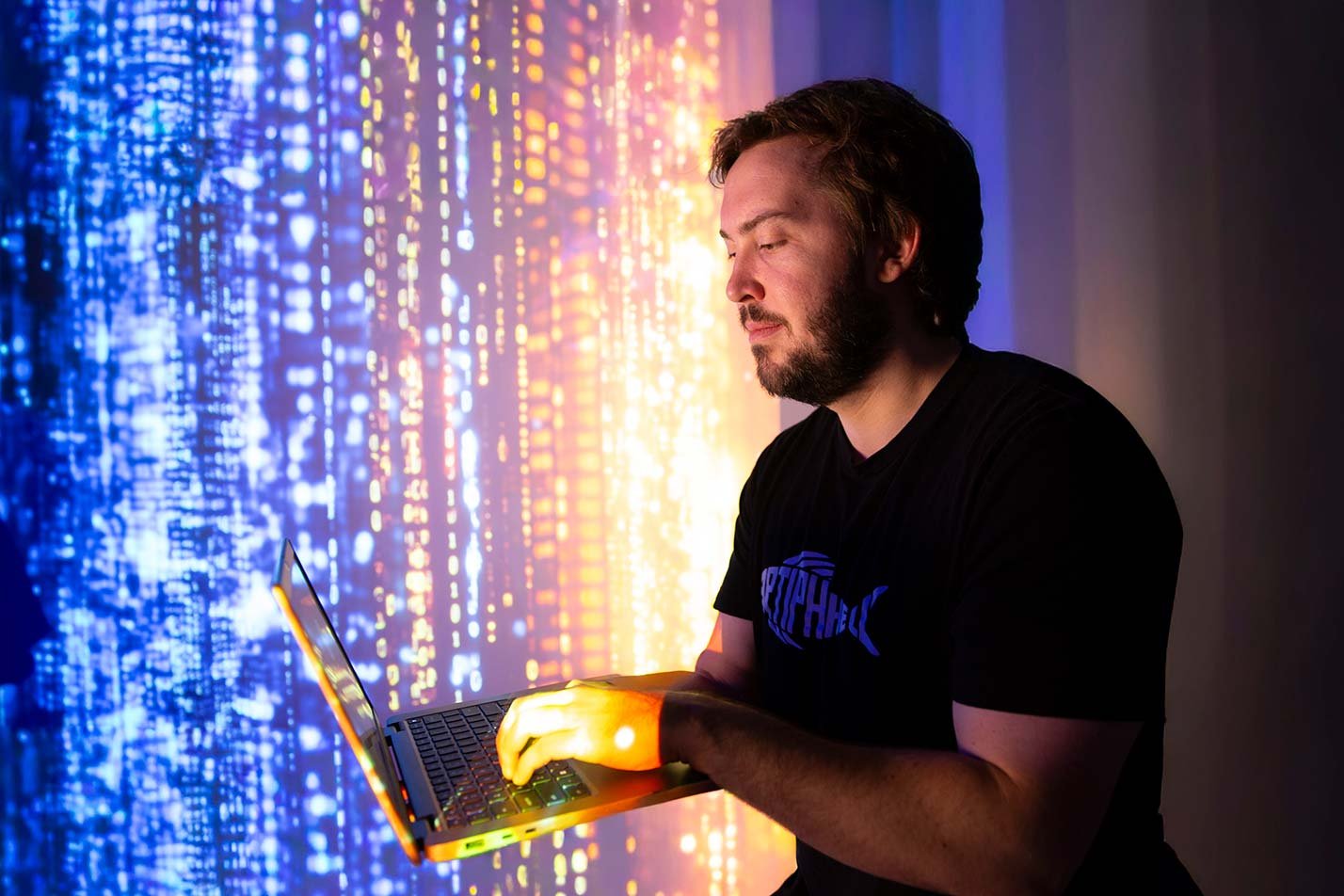 A laptop glows under colorful digital light patterns, symbolizing the tech environment in ASU's Artificial Intelligence and Machine Learning degree.