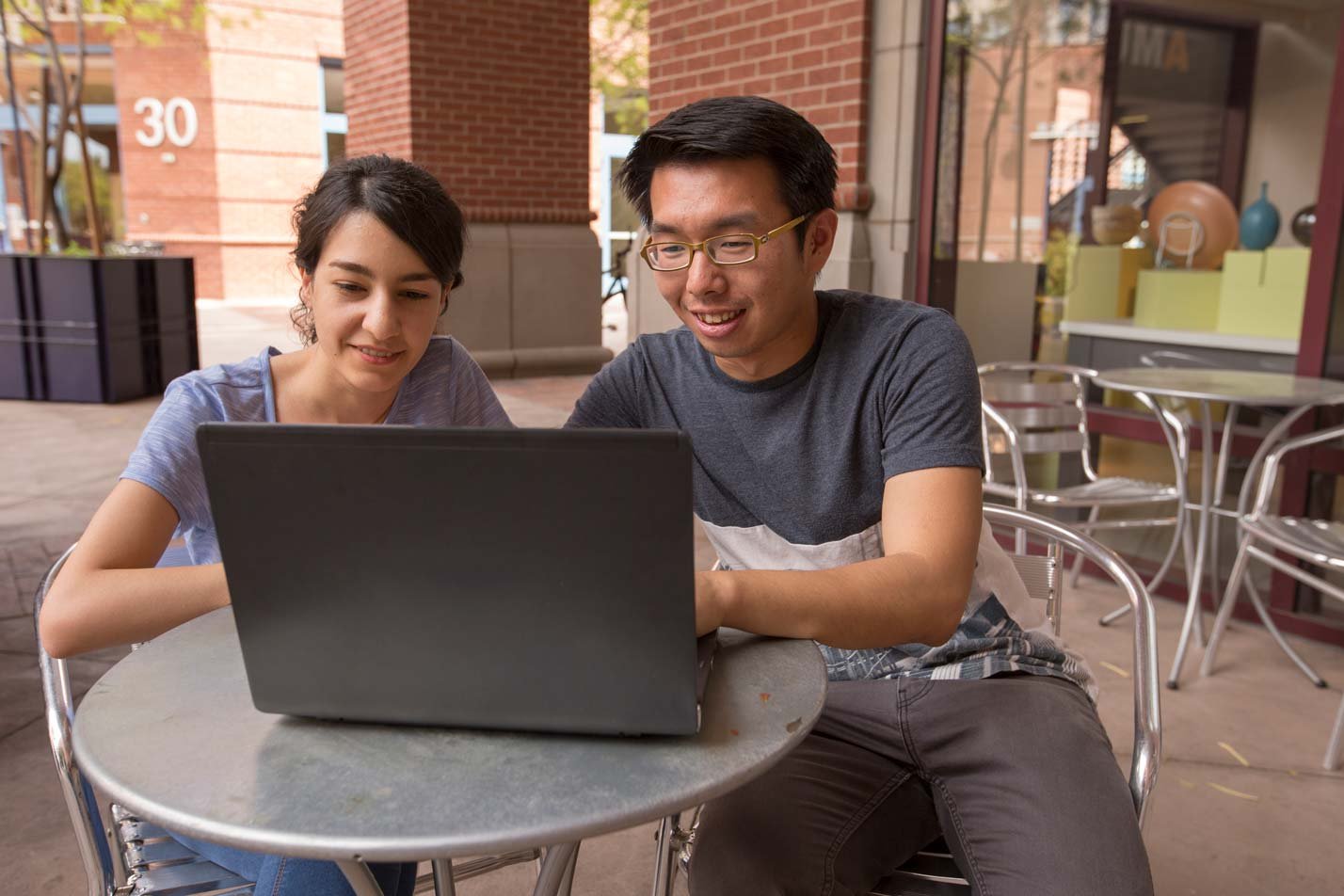 Students collaborating at a café table with a laptop, showcasing teamwork and innovation in ASU's MS in Artificial Engineering program.