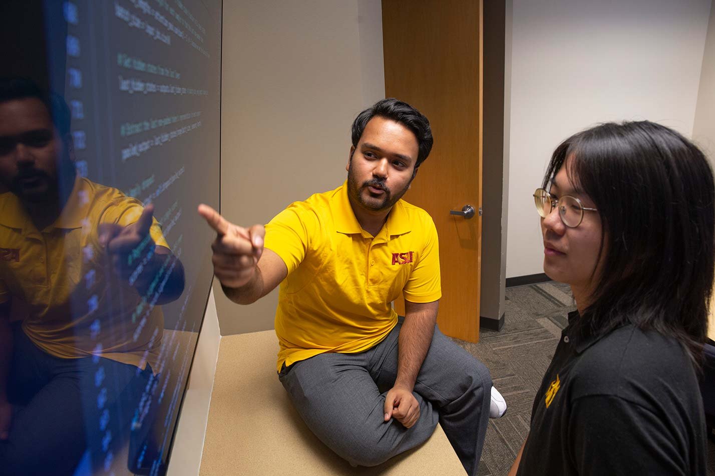 Two students discuss programming concepts over on-screen code, exemplifying learning in ASU's Computer Engineering program.