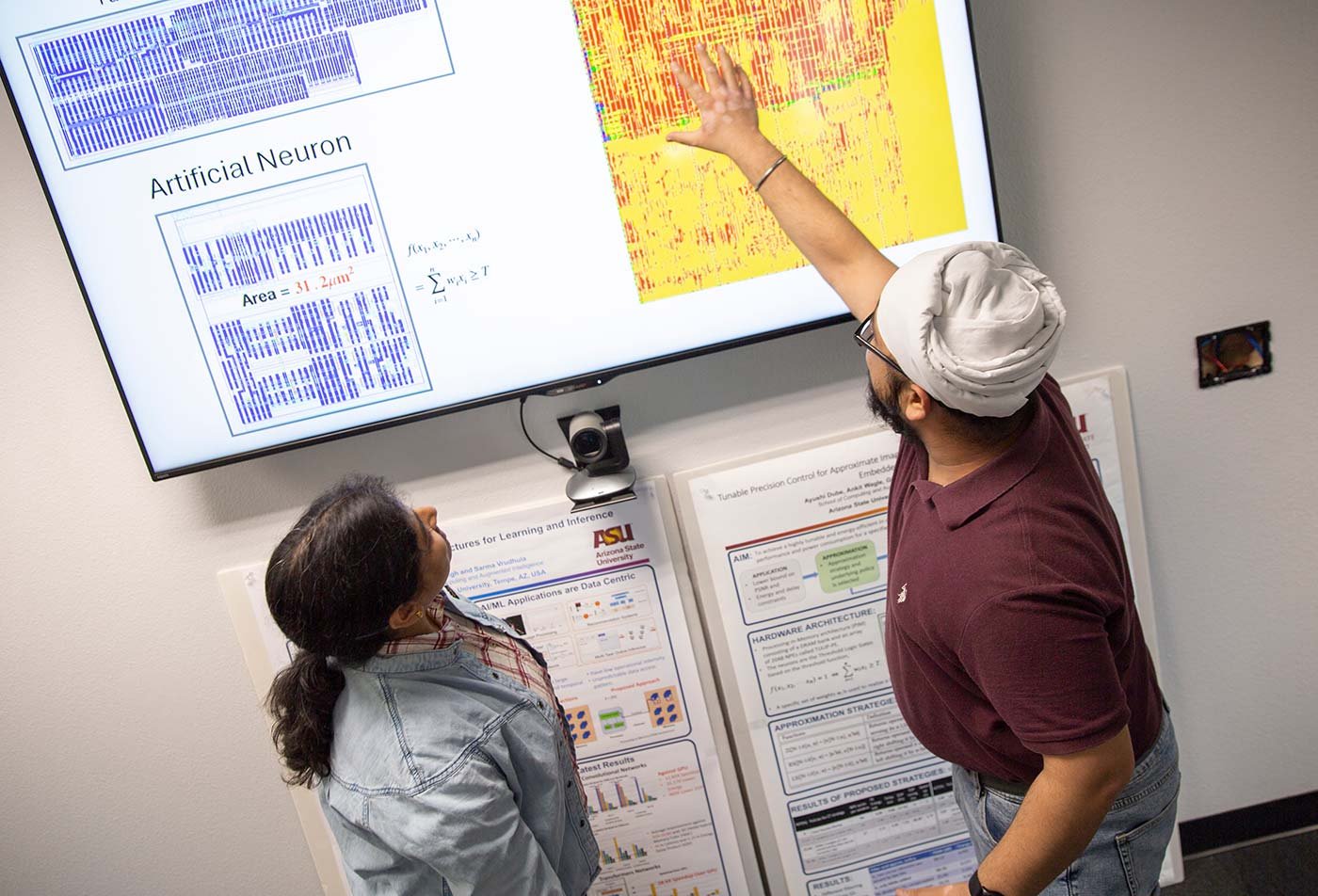 A discussion unfolds around a screen showing chip design and neural network diagrams in ASU's PhD in Computer Engineering program.