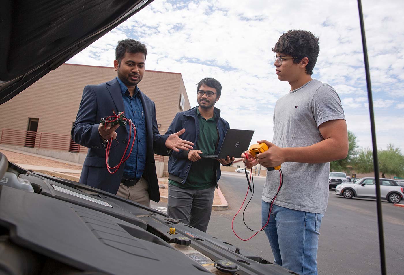 A professor explains electrical components to students beside an electric car, reflecting ASU's Clean Energy Systems PhD program.