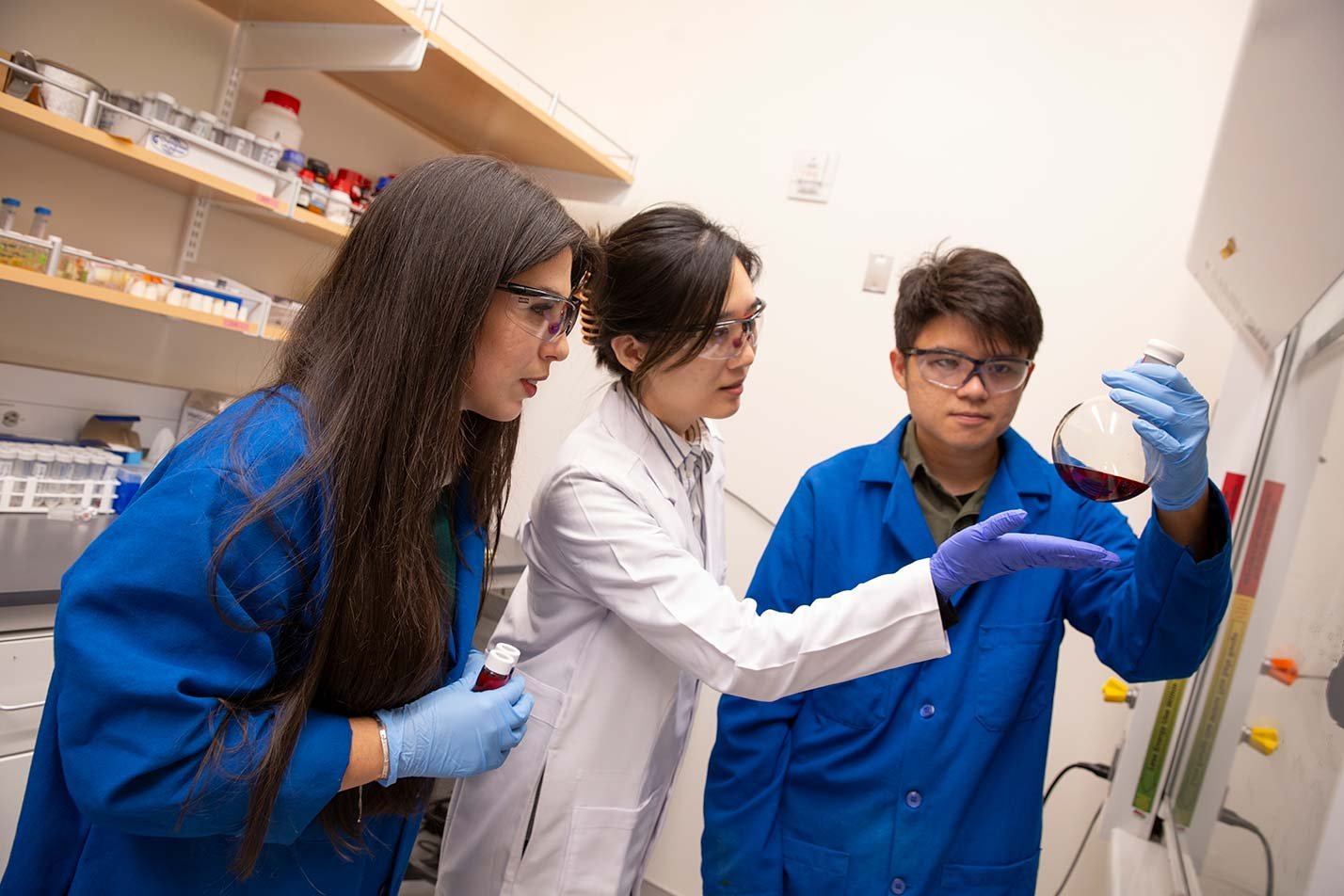 Students in lab coats examine a chemical solution in a laboratory, illustrating hands-on learning in ASU's Chemical Engineering degree.