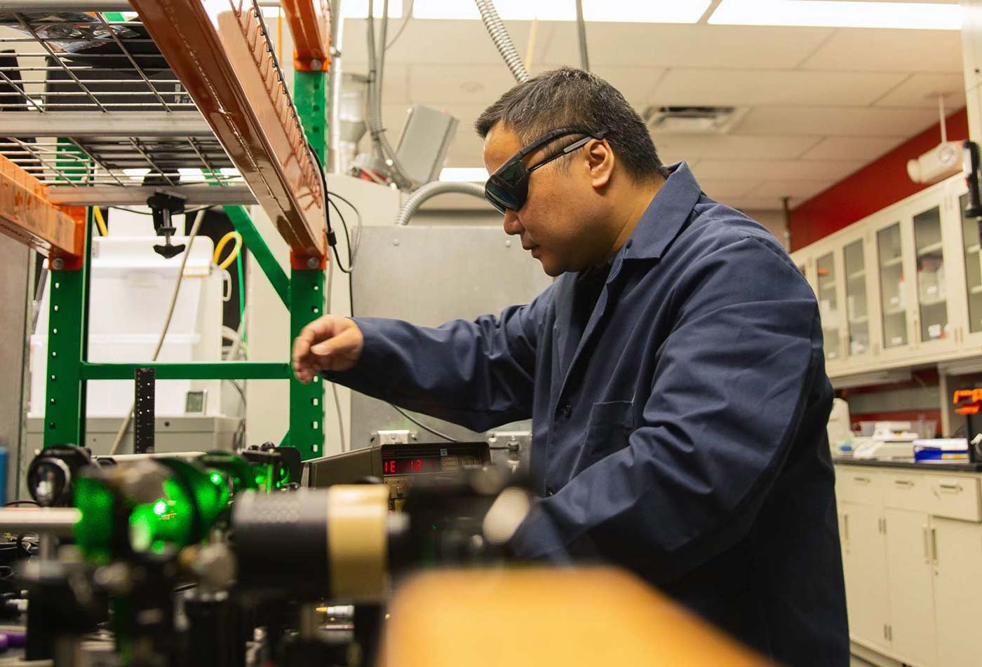 A researcher in goggles and a lab coat adjusts equipment amid green laser lights in ASU's Chemical Engineering program.