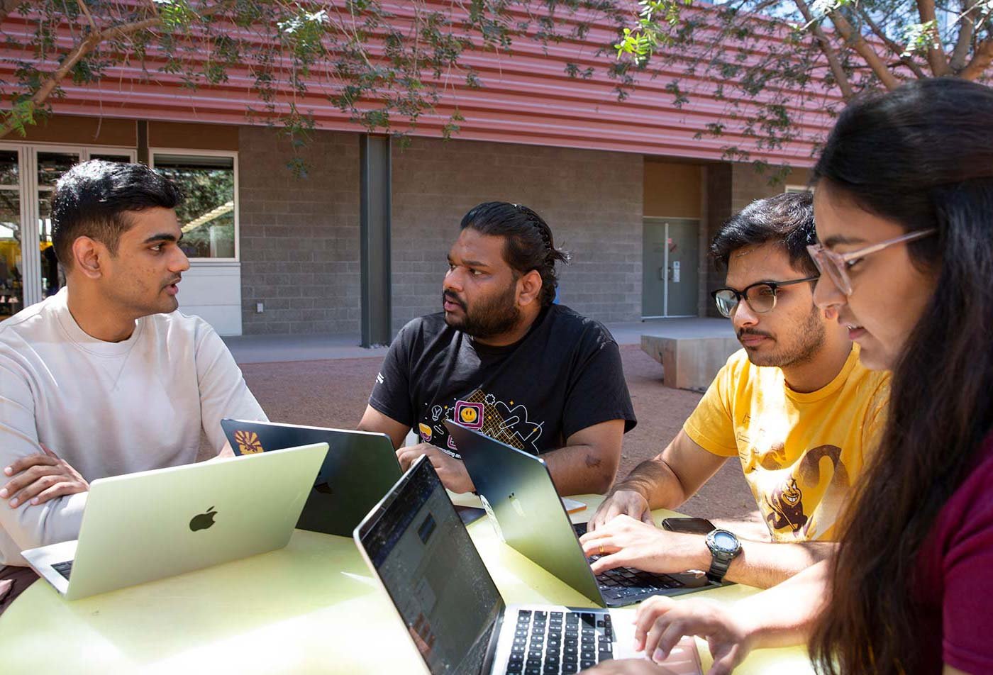 Students focus on their laptops in a collaborative outdoor setting, highlighting teamwork in ASU's Computer Science and Artificial Intelligence degree.
