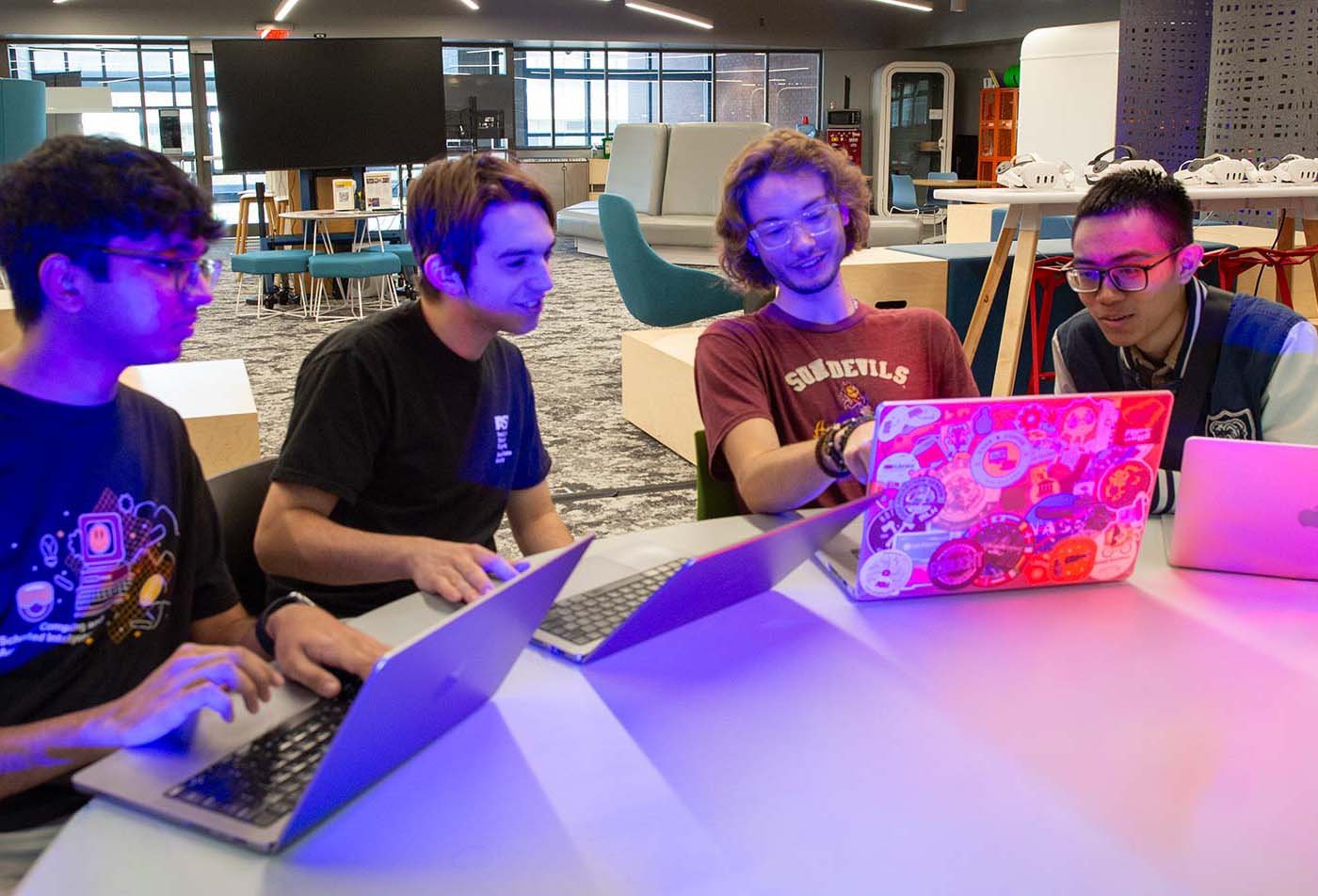 Students collaborate on coding at a modern workspace, showcasing teamwork and creativity in ASU's Computer Science (Artificial Intelligence) program.