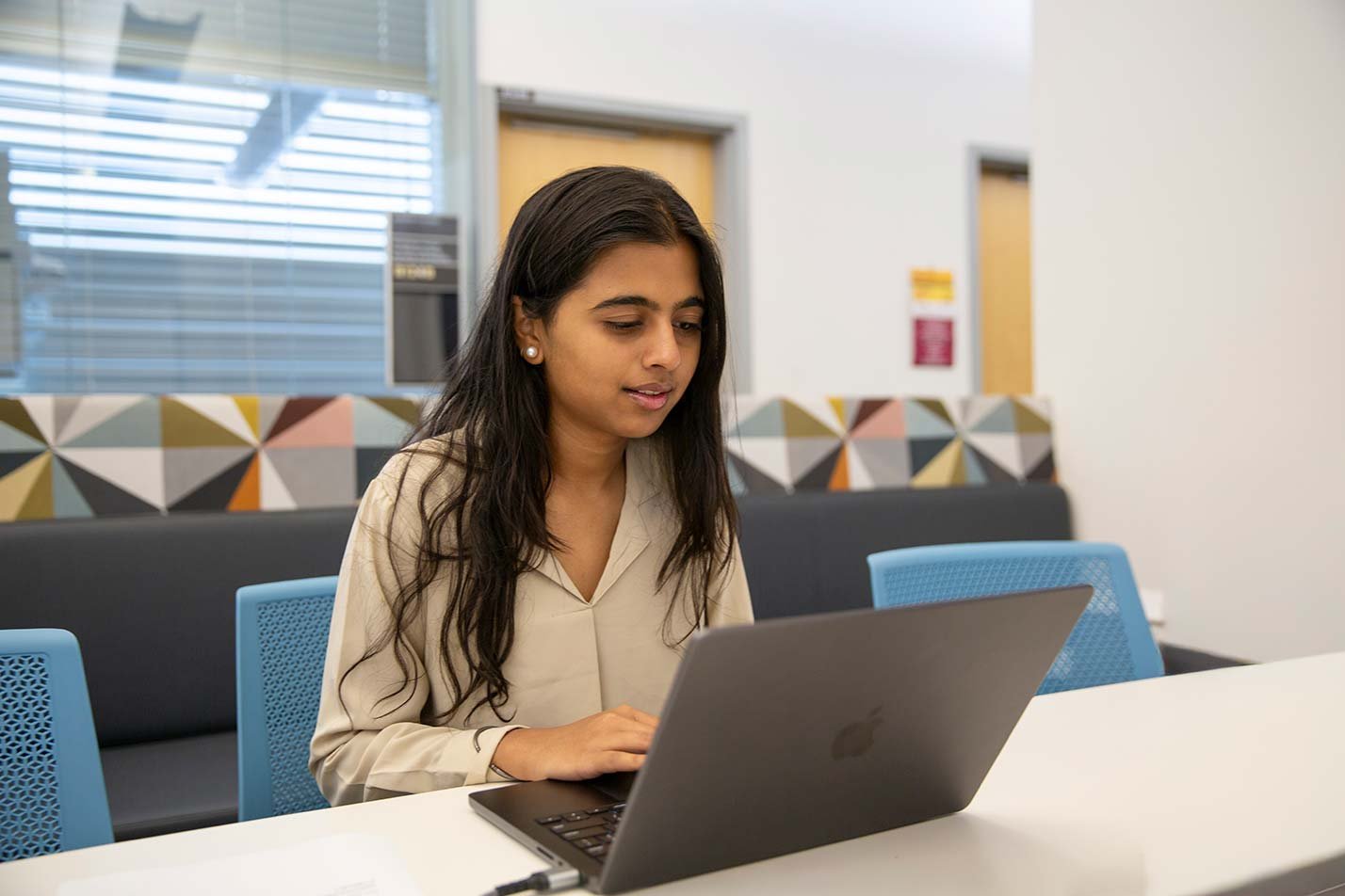 A focused student types on a laptop in a modern study space, showcasing engagement in ASU's Computer Systems Engineering program.