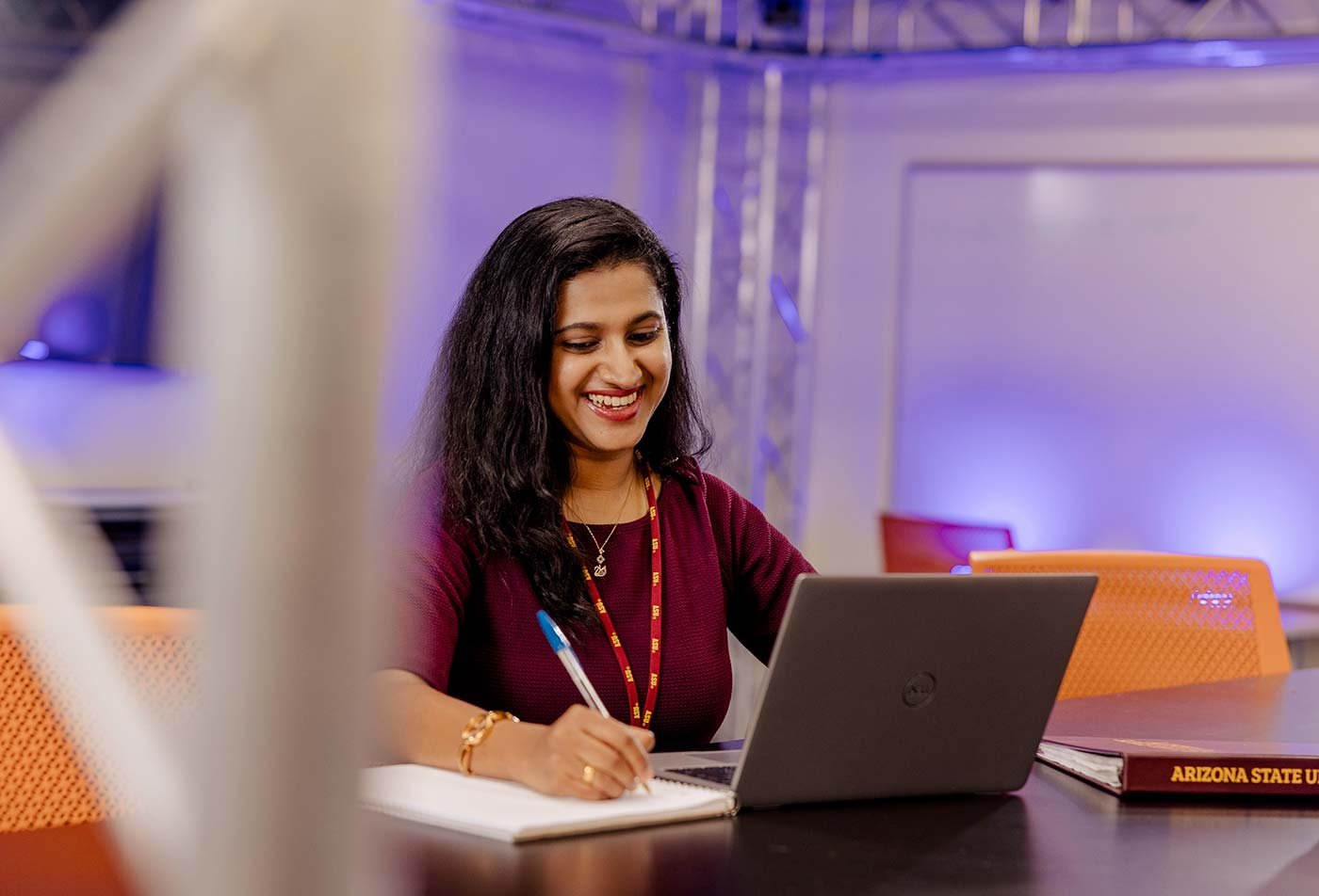 A smiling student works on a laptop in a collaborative study space, reflecting hands-on learning in ASU's Computer Science (Cybersecurity) degree.