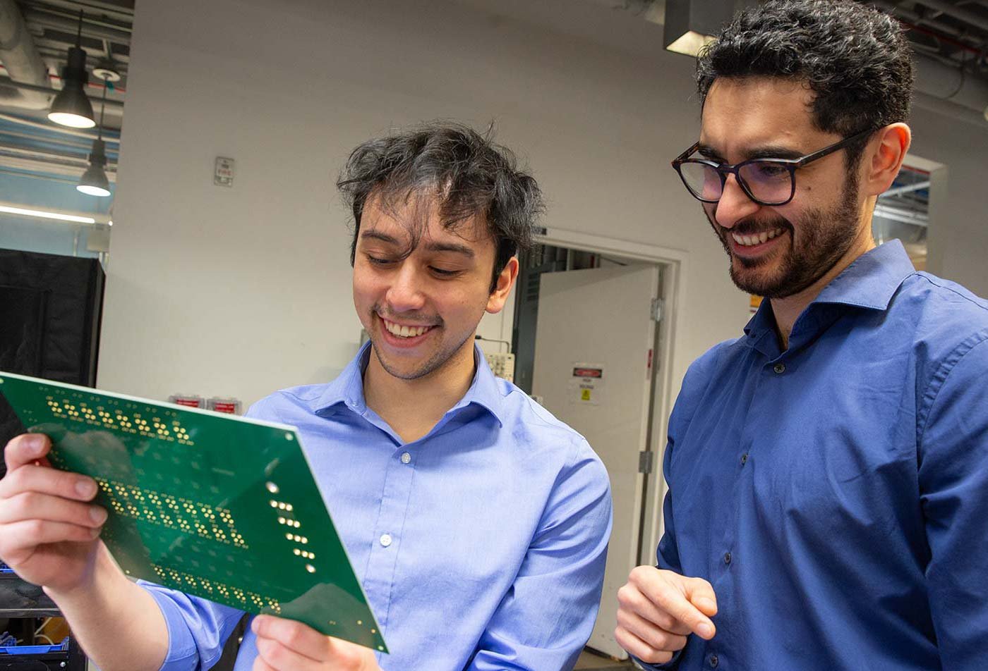A student discusses a circuit board with a professor in an engineering lab, reflecting hands-on learning in ASU's Electrical Engineering program.
