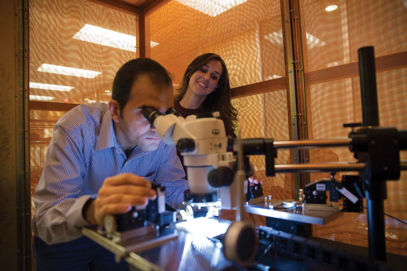 Researchers use a precision optical instrument in a laboratory, highlighting advanced experimentation in ASU's Electrical Engineering, MS degree.