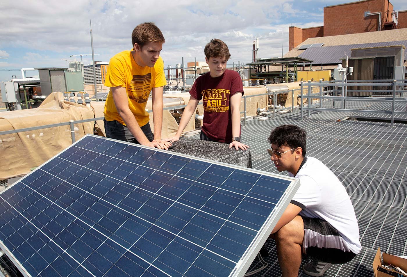 Three students gather around a rooftop solar panel, collaborating on a clean energy project in ASU's BSE Engineering (Clean Energy Systems) degree.