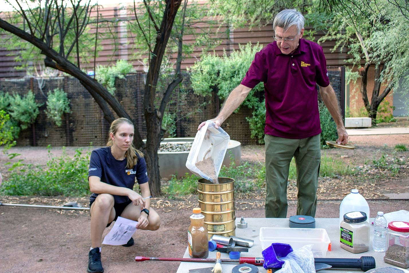 A professor pours soil samples into a sieve as a student observes, demonstrating skills in ASU's Environmental and Resource Management program.
