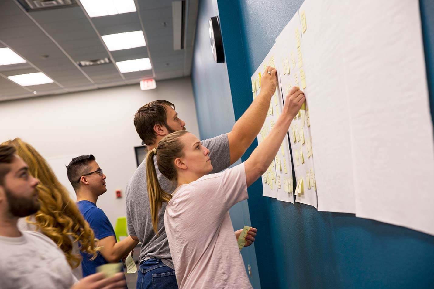 A group collaborates with sticky notes on a classroom wall, showcasing teamwork in ASU's Graphic Information Technology (User Experience) program.