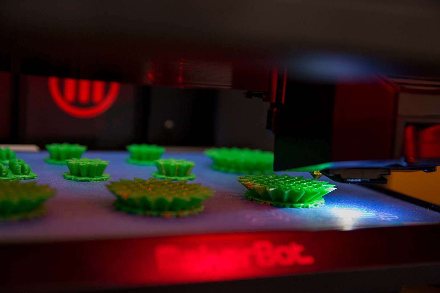 A 3D printer produces vibrant green widgets, showcasing innovative technology relevant to ASU's BSE Industrial Engineering program.