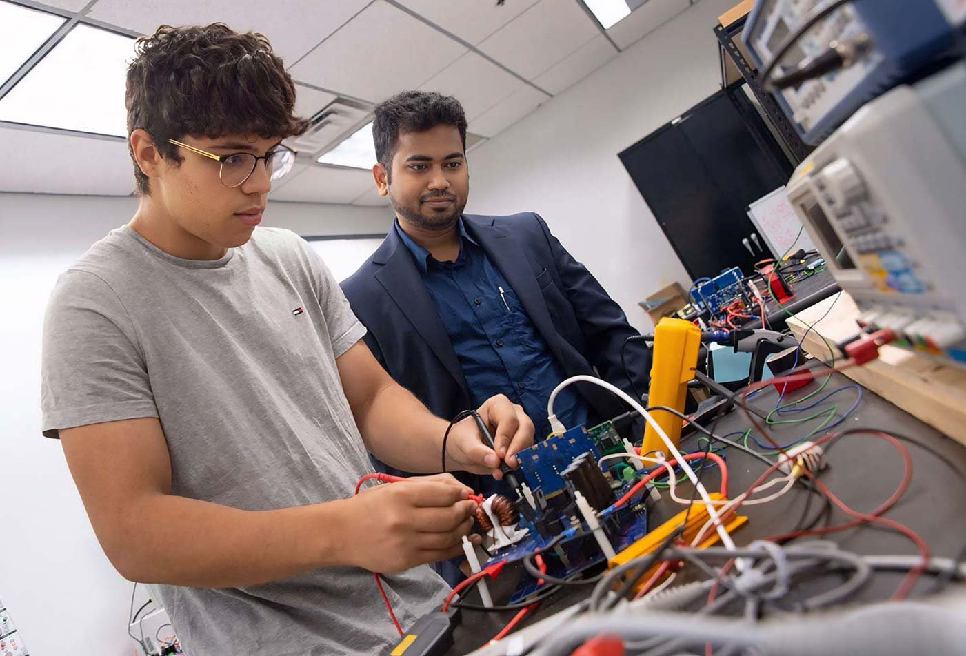 A student works on a circuit board, guided by a professor, highlighting collaborative learning in ASU's Mechanical Engineering program.