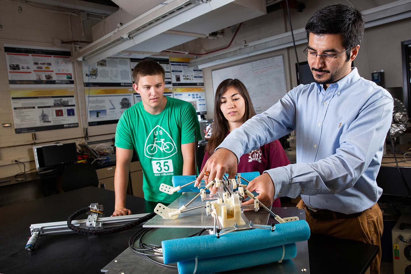 A professor explains a mechanical device to students in a lab, illustrating practical learning in ASU's Mechanical Engineering degree program.