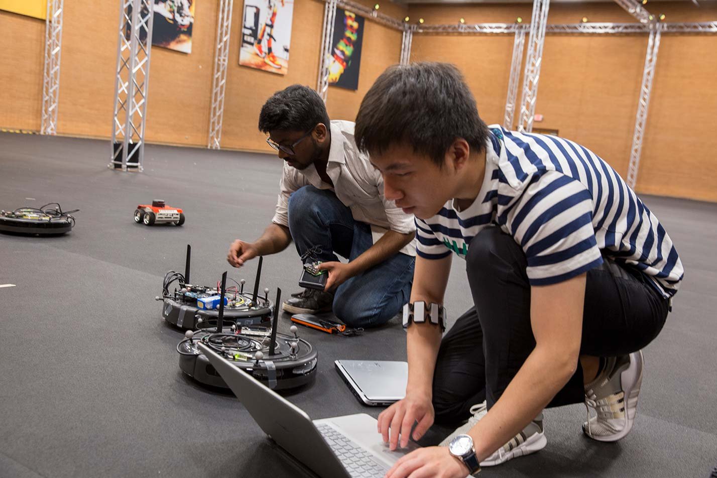 Two students work on robots in a demonstration arena, illustrating collaboration and innovation in ASU's Robotics and Autonomous Systems degree.