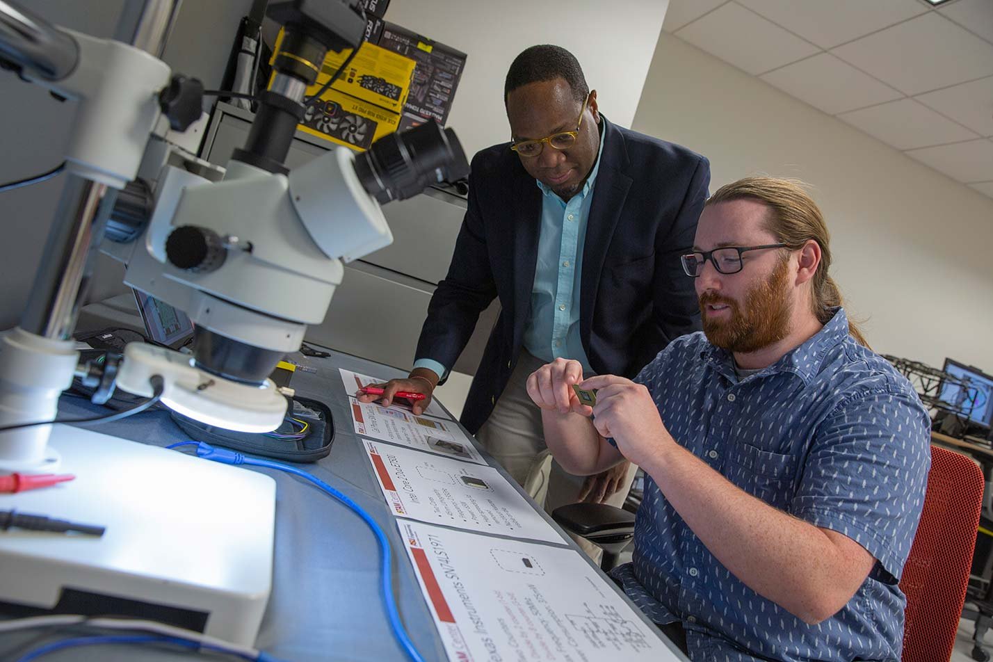 Researchers inspect components under a microscope, highlighting cleanroom techniques in ASU's Semiconductor Processing (Graduate Certificate).