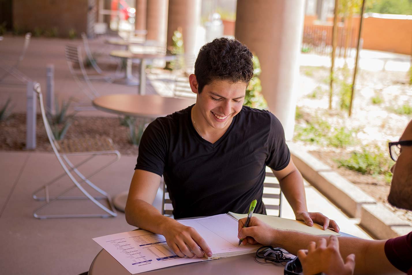 A student smiles while talking with another student and taking notes, illustrating collaboration in ASU's Technological Entrepreneurship and Management program.