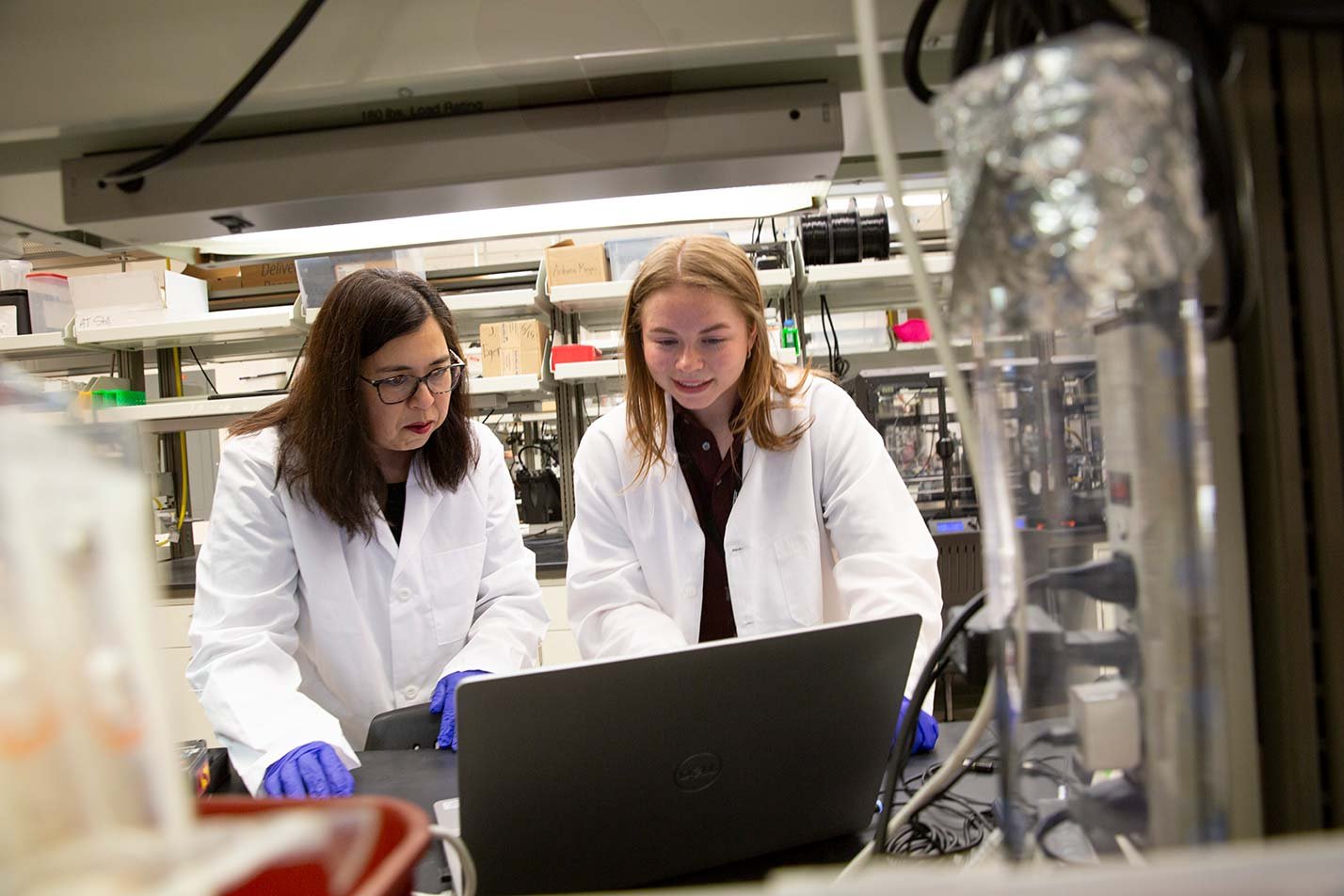 Two researchers in lab coats and gloves collaborate over a laptop, exemplifying teamwork in ASU's Biological Design PhD program.