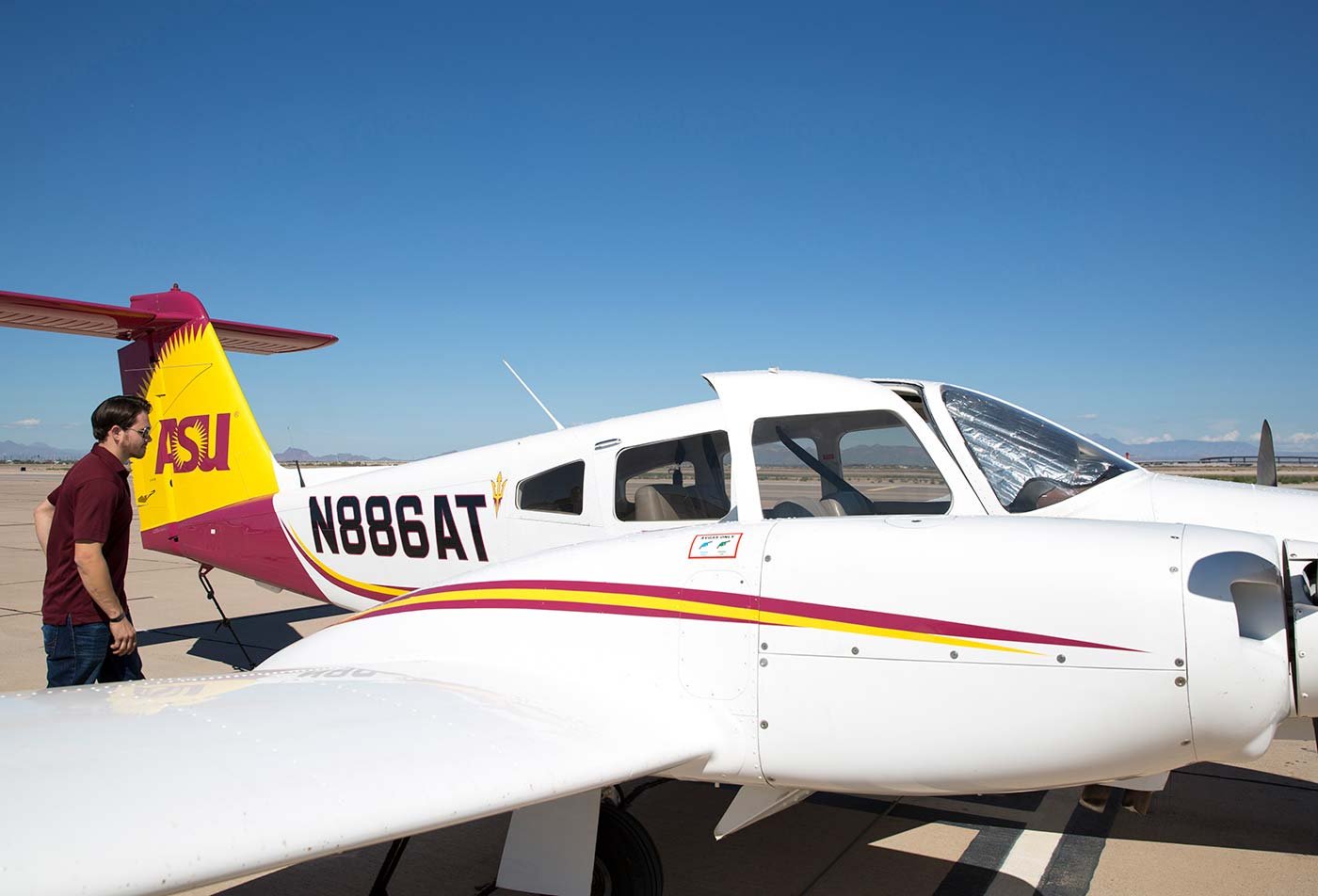 A student inspects an ASU-branded airplane on a clear day, showcasing practical involvement in ASU's Aeronautical Management Technology (Air Transportation Management) degree.