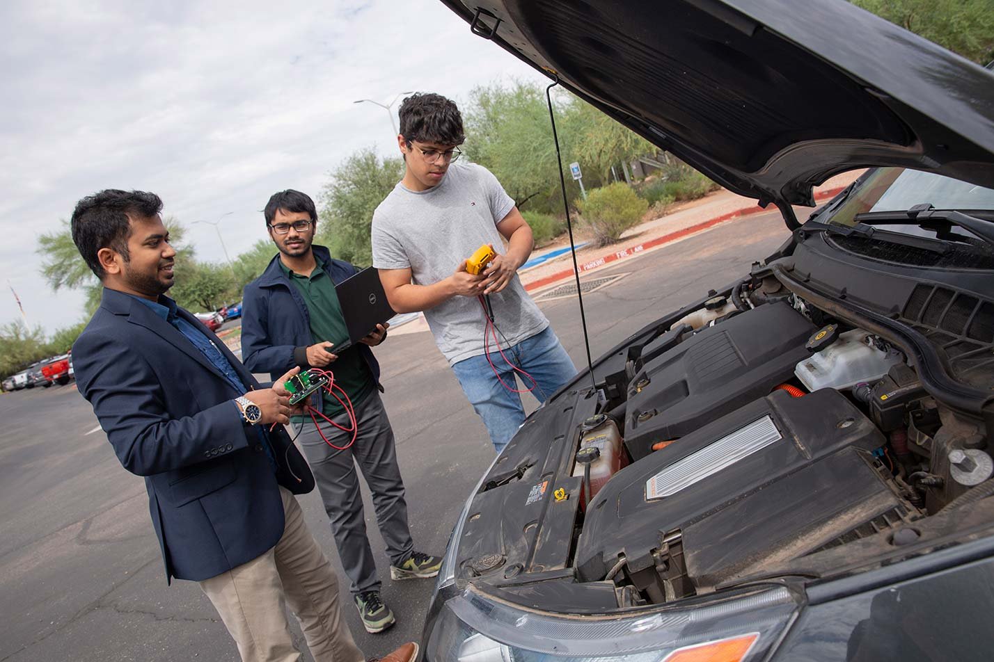 A group of students reviews automotive components under the hood of a car, showcasing practical learning in ASU's Automotive Systems degree.