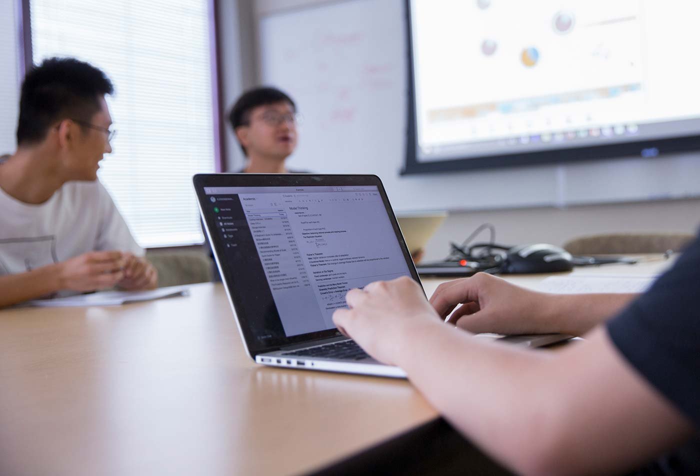 Collaborative discussion among students as one types at a laptop, showcasing teamwork in ASU's Applied Science (Operations Management) program.