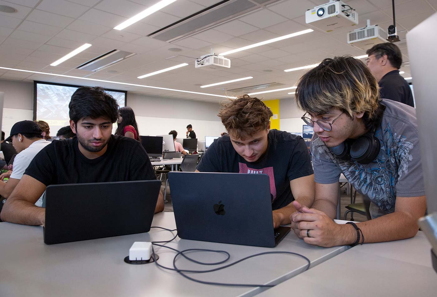 Three students collaborate around laptops in a modern classroom, showcasing teamwork in ASU's Software Engineering degree.
