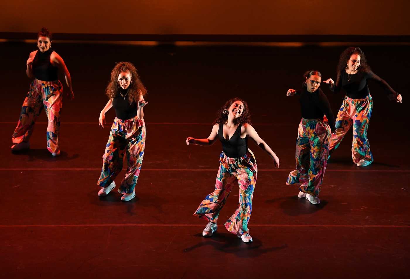 Students dance on a stage light with dramatic lighting, showcasing the field explored in the Dance, MFA.