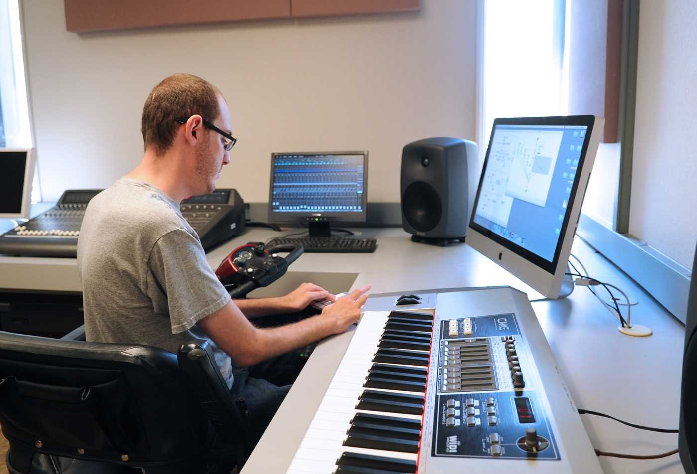 A student works with sound equipment, a computer and a music keyboard, reflecting hands-on learning in the Composition (Interdisciplinary Digital Media), MM.