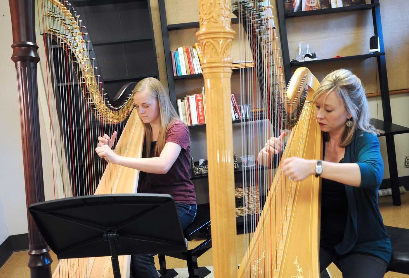 Two students play the harp together, demonstrating the field explored in the BMUS in Performance (Orchestral Instrument).