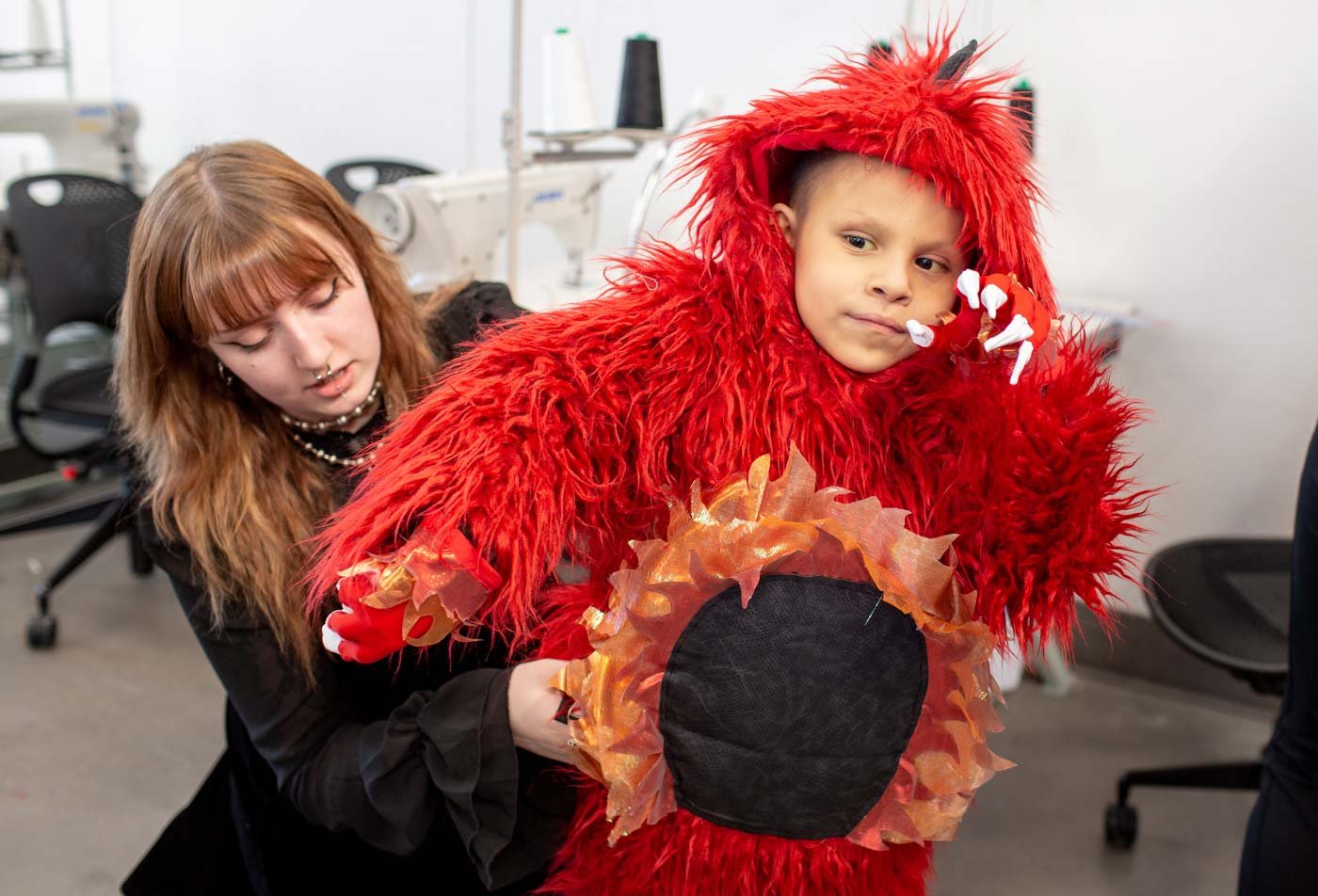 A fashion student helps a child into a red monster costume, showcasing the field explored in the BFA in Costume Design and Technology for the Creative Industries.