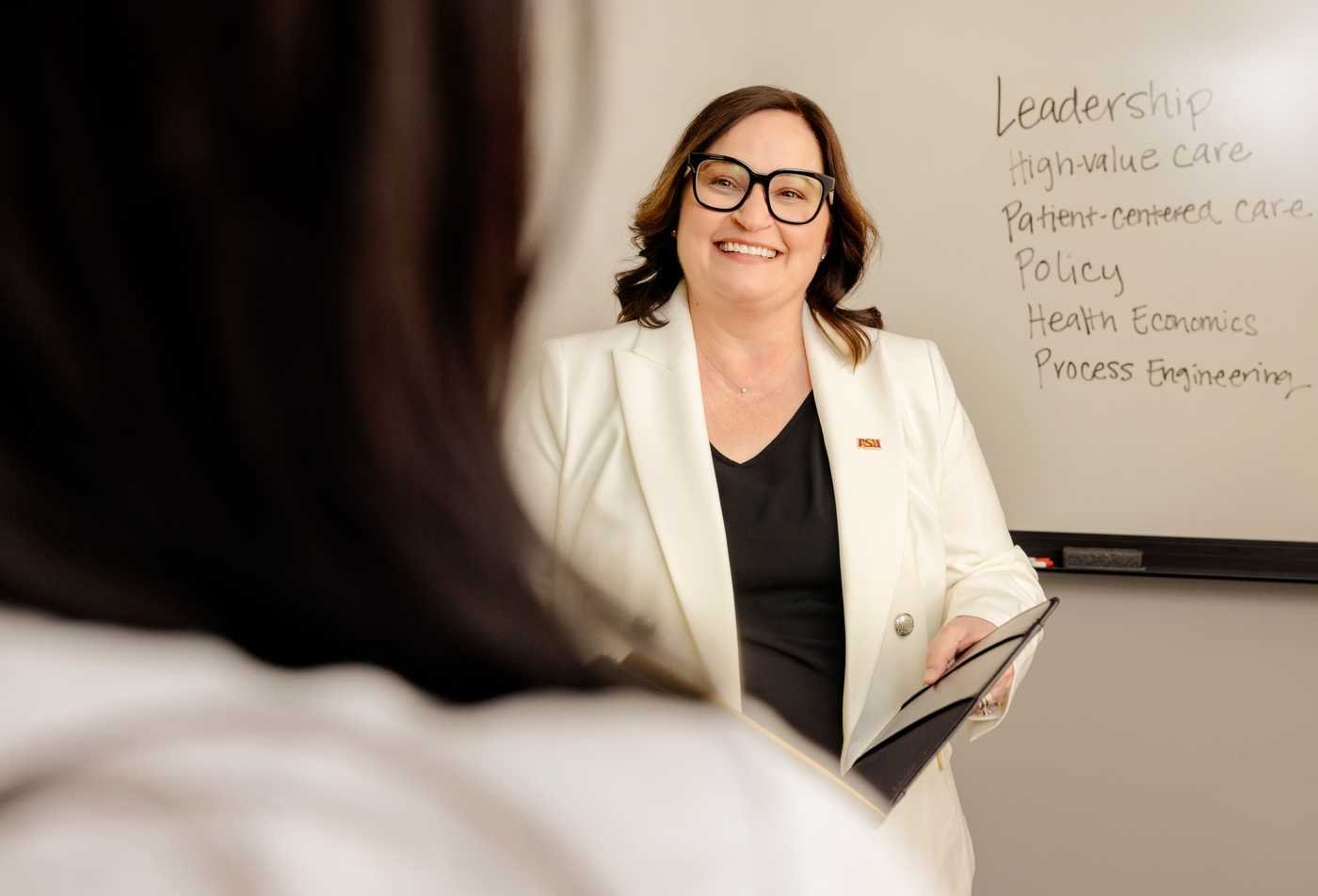 A researcher in a lab coat explains heath care administration to a student, showcasing the collaborative learning in the MS in Health Care Administration and Policy.