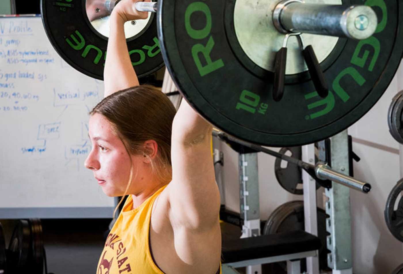 A student lifts weights, showing the principles explored in BS in Sports Science and Performance Programming.