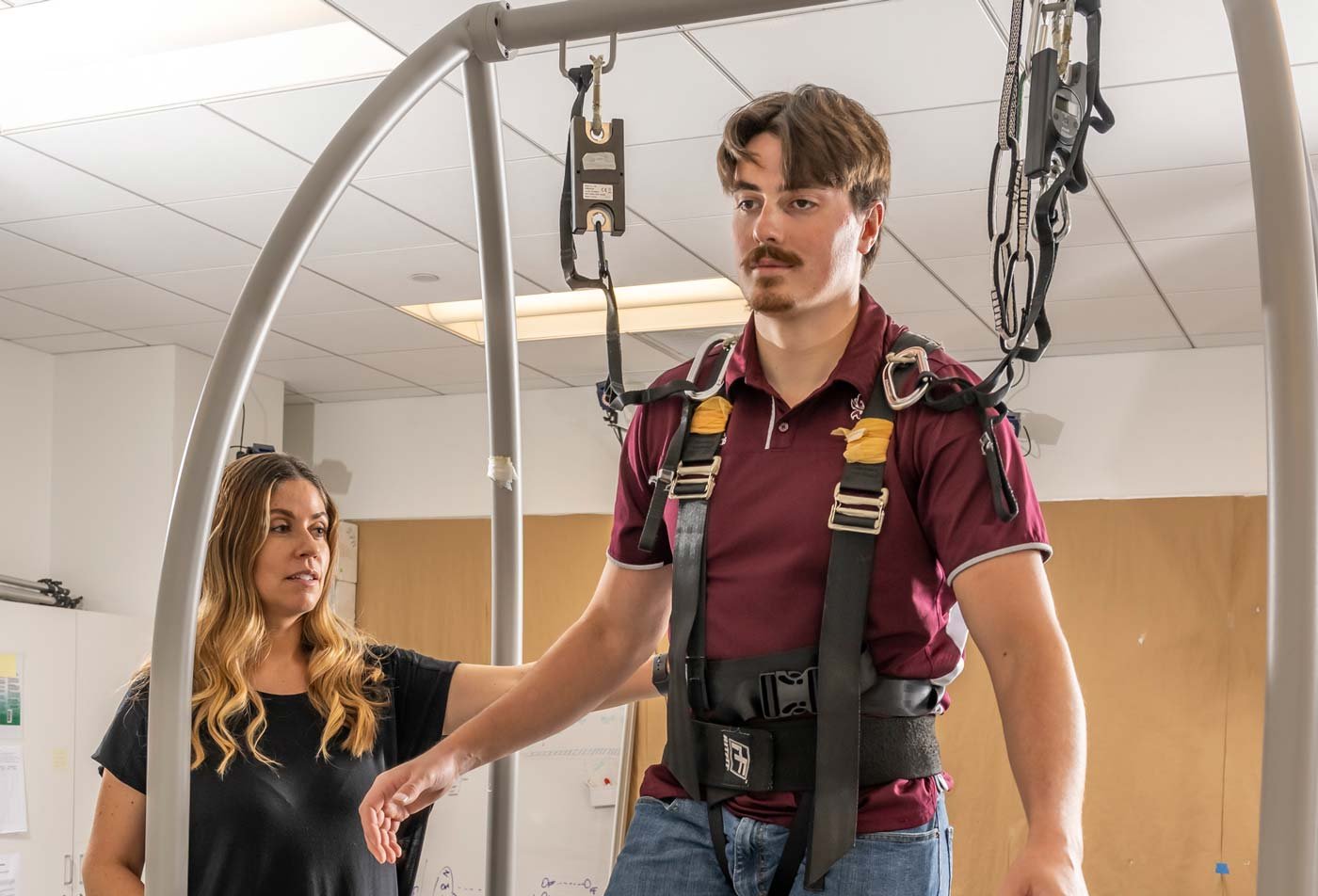A student and faculty member run an experiement on a body support harness on a treadmill in a rehabilitation setting, showcasing the hands-on learning in the BS in Kinesiology.