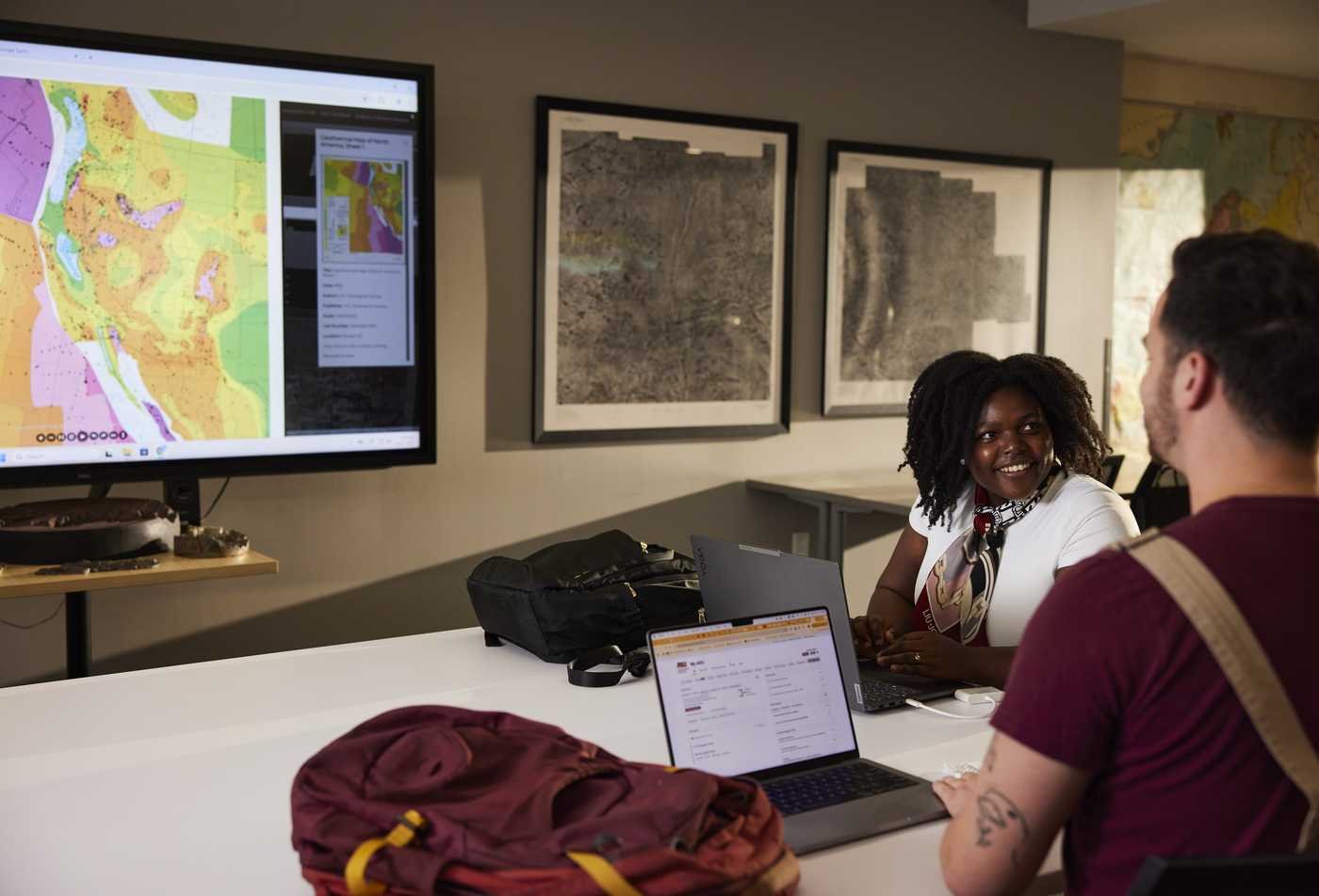 Two students discuss a digital map displayed on a classroom screen, demonstrating hands-on learning in the Urban Planning.