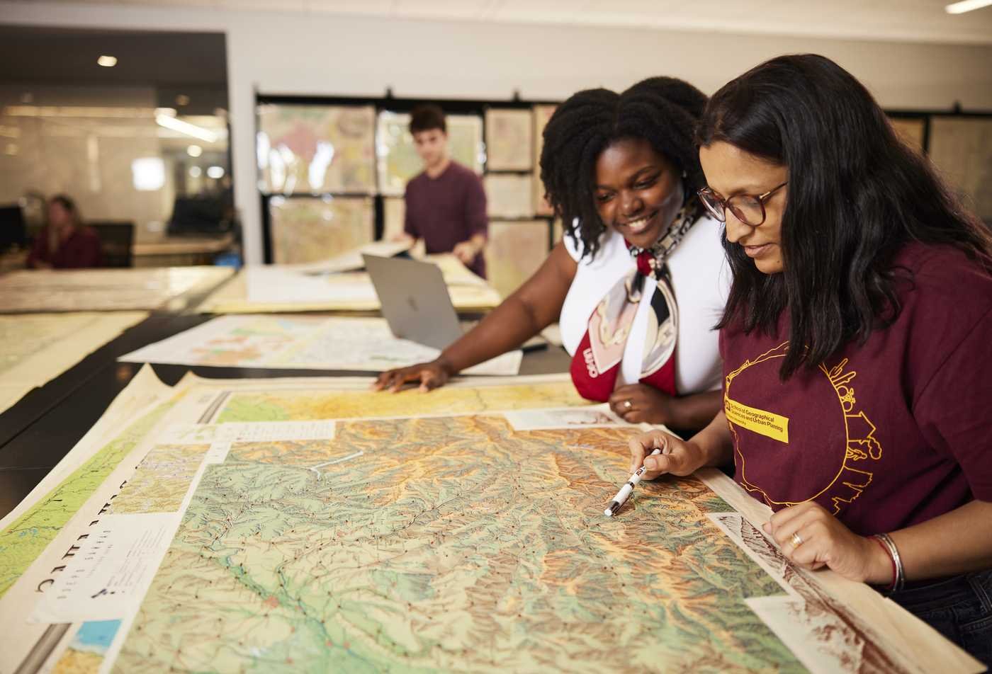 Students examine a large topographic map together in a map library, demonstrating hands-on learning in the Urban Planning, PhD.