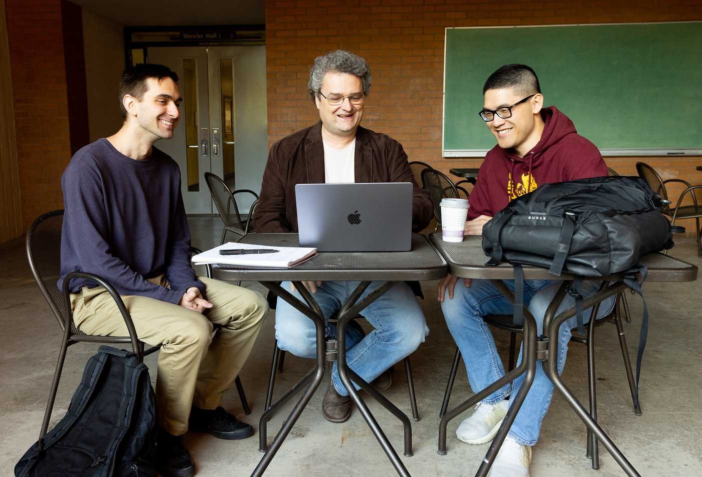 Two students sit with a faculty member while they examine a laptop, showcasing hands-on learning in the Statistics and Data Science (Graduate Certificate).