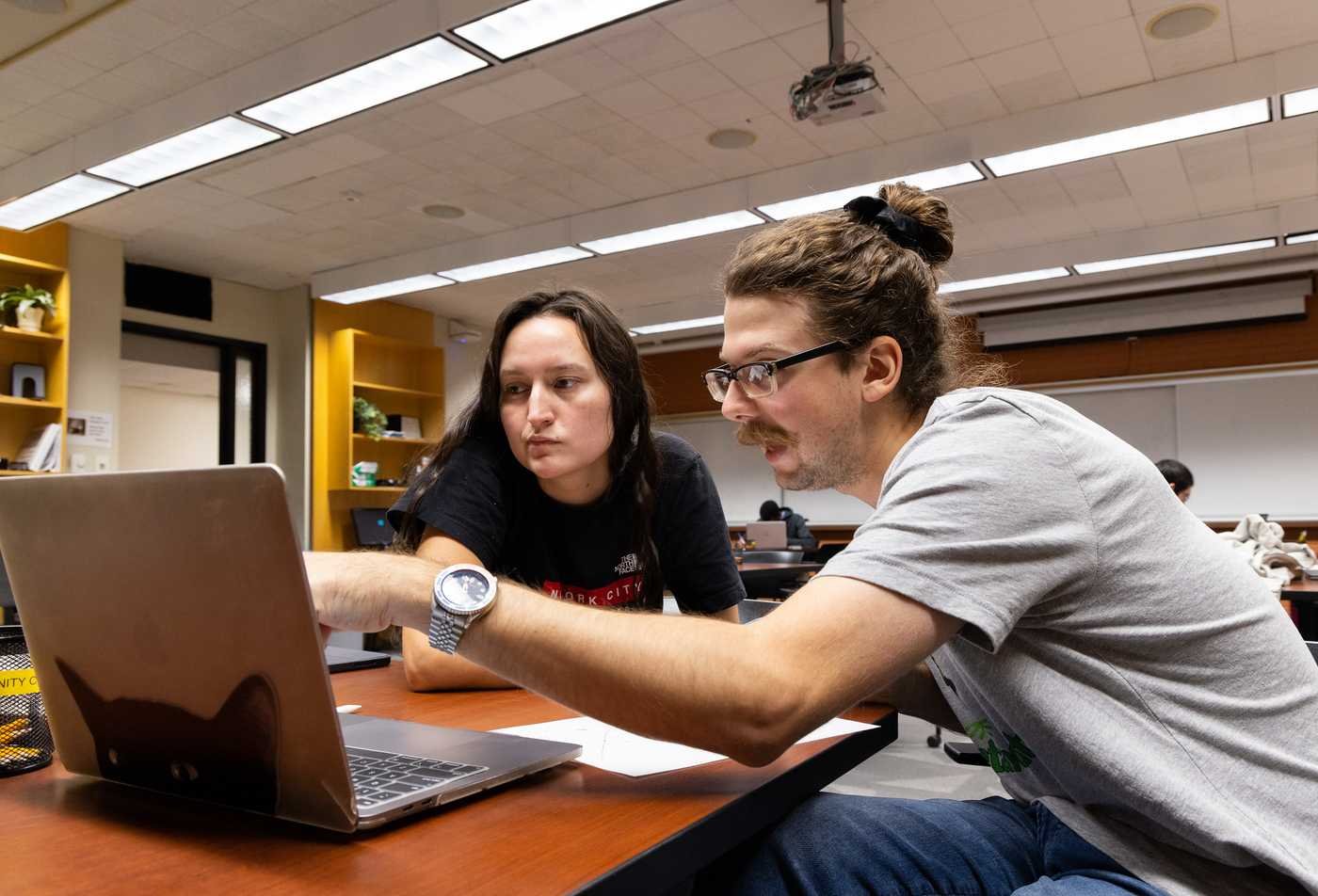 Two students look at a laptop together, showcasing hands-on learning in the Statistics, MS.