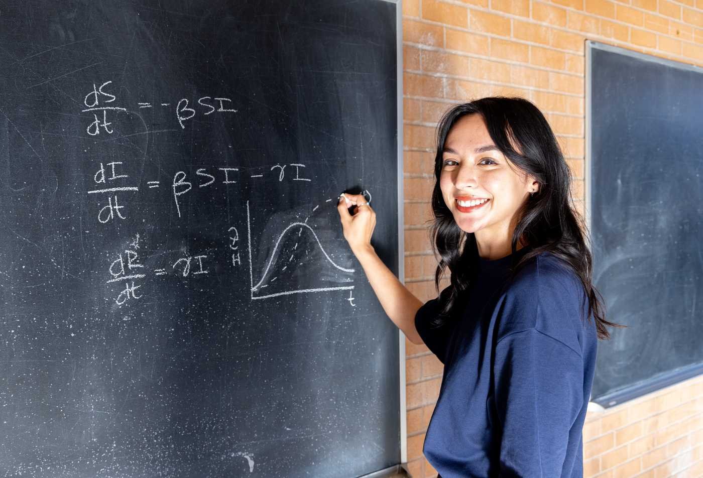 A student writes math equations on a chalkboard, demonstrating the knowledge gained in the PhD in Applied Mathematics.