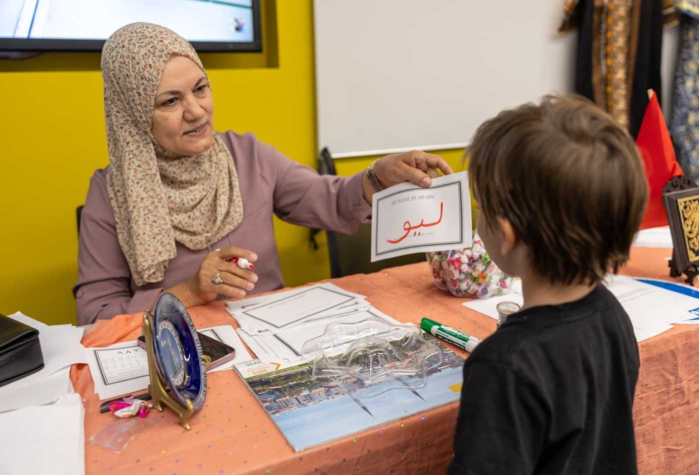 A student demonstrates Arabic to a young boy at an event, showcasing the expertise in certificate in Arabic Studies.