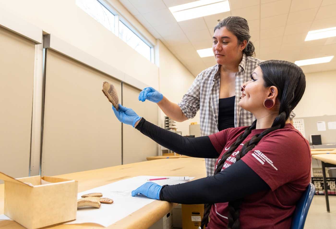 An anthropology student examines a piece of Indigenous pottery with a professor, demonstrating the hands-on learning in the BA in Anthropology.