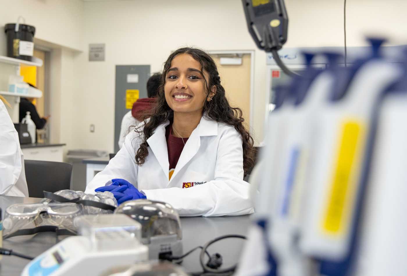 A student smiles while working and learning in her lab, reflecting hands-on discovery in the PhD in Biochemistry.